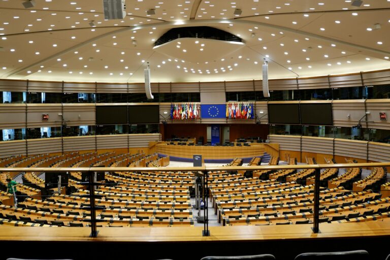 Interior of the European Parliament chamber showing the semicircular seating arrangement and EU flags, illustrating how the EU works