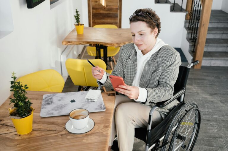 Professional woman in wheelchair working on smartphone in a café, illustrating workplace accessibility under the European Accessibility Act